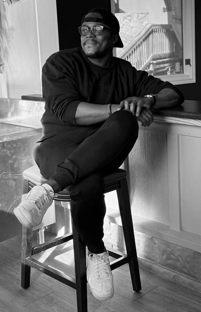 Black and white portrait of Ajar, Adewole Jonathan Alitonou, seated and looking to the side.